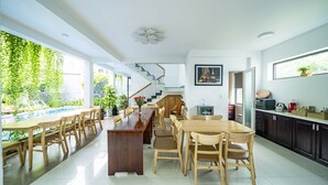 A spacious dining area with a long wooden table and chairs, a kitchen with dark cabinets, and a staircase leading to an upper level. - My Anh Boutique Villa Hoi An (Da Nang)