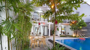 A poolside area with a table and chairs, surrounded by bamboo plants and a building with balconies. - My Anh Boutique Villa Hoi An (Da Nang)