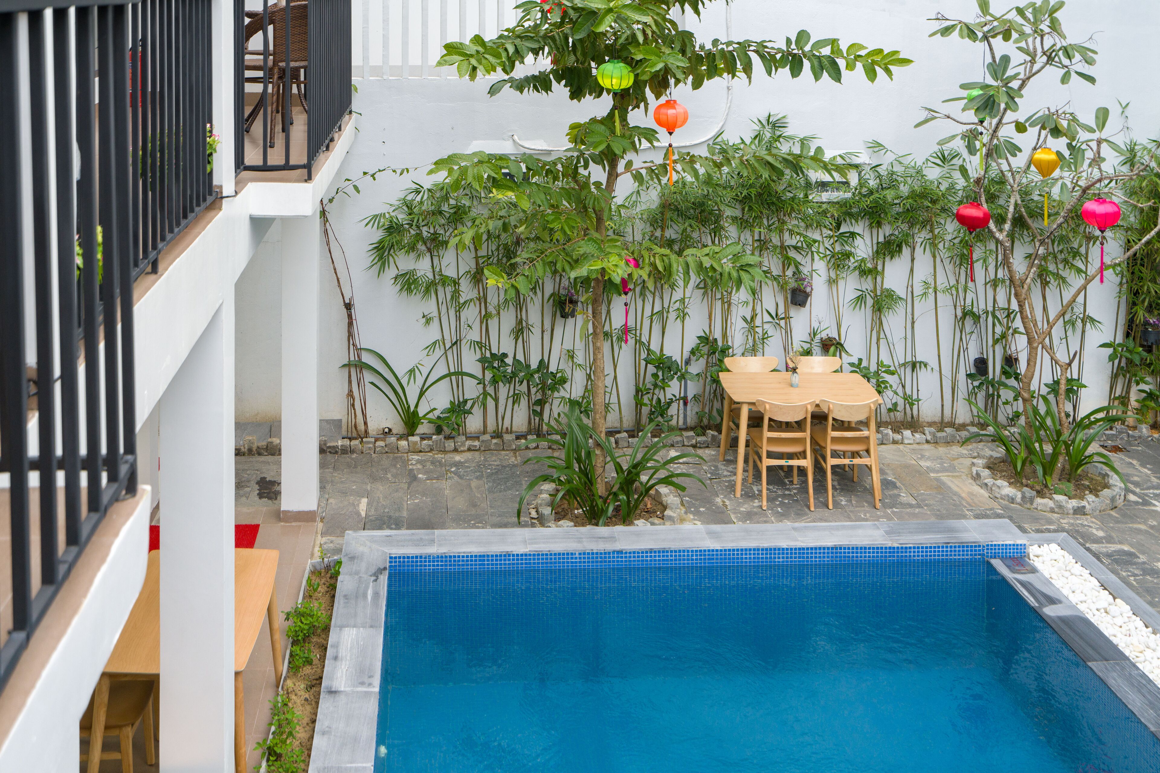 A pool area with a tiled edge, surrounded by potted plants and a wooden table with chairs.