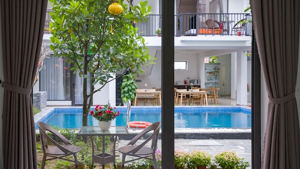 A room with a view of a swimming pool, dining area, and a balcony with outdoor furniture. - My Anh Boutique Villa Hoi An (Da Nang)