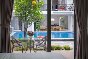 A room with a view of a swimming pool, dining area, and a balcony with outdoor furniture. - My Anh Boutique Villa Hoi An (Da Nang)