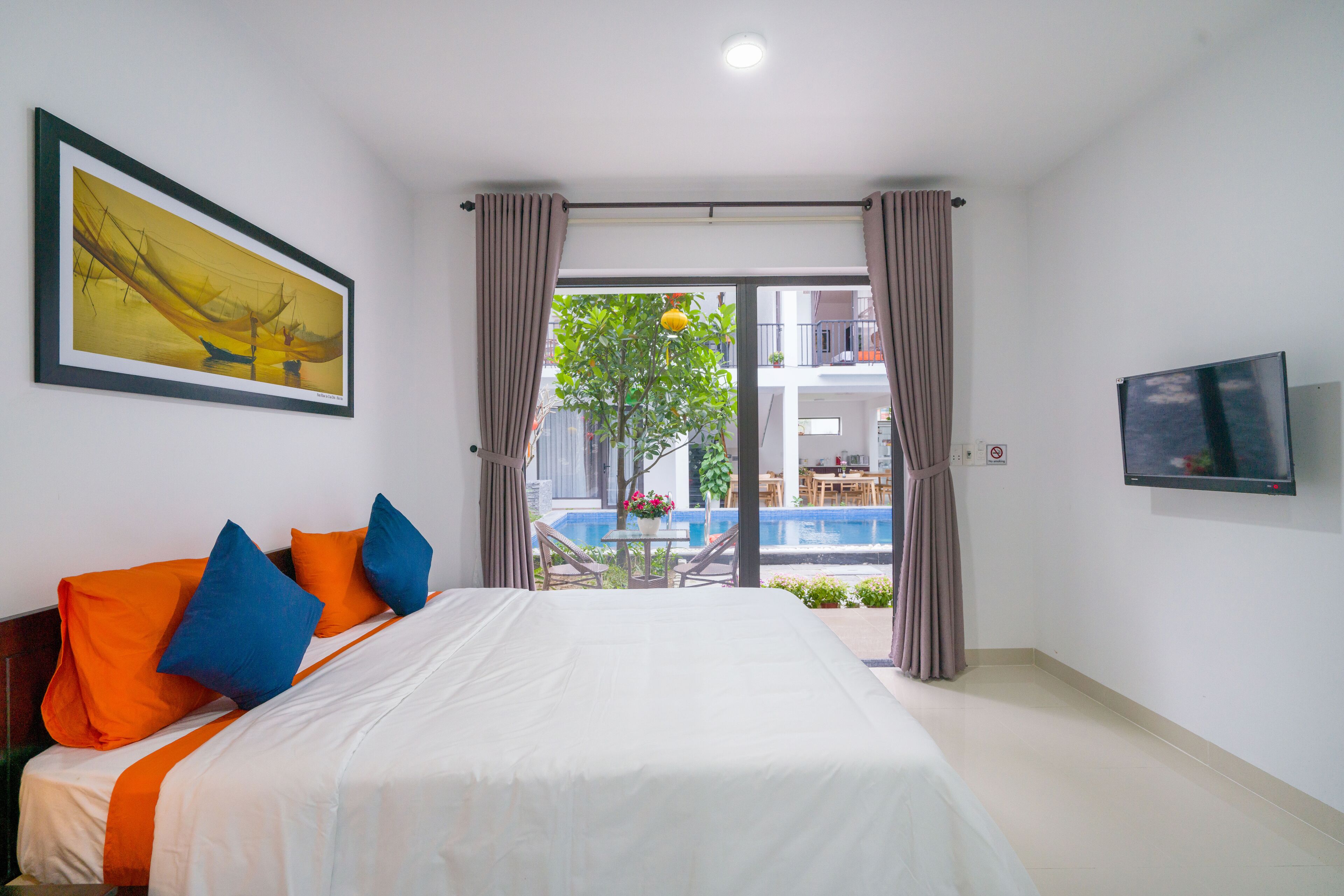 A hotel room with a bed, a TV, a painting, and a view of an outdoor swimming pool.