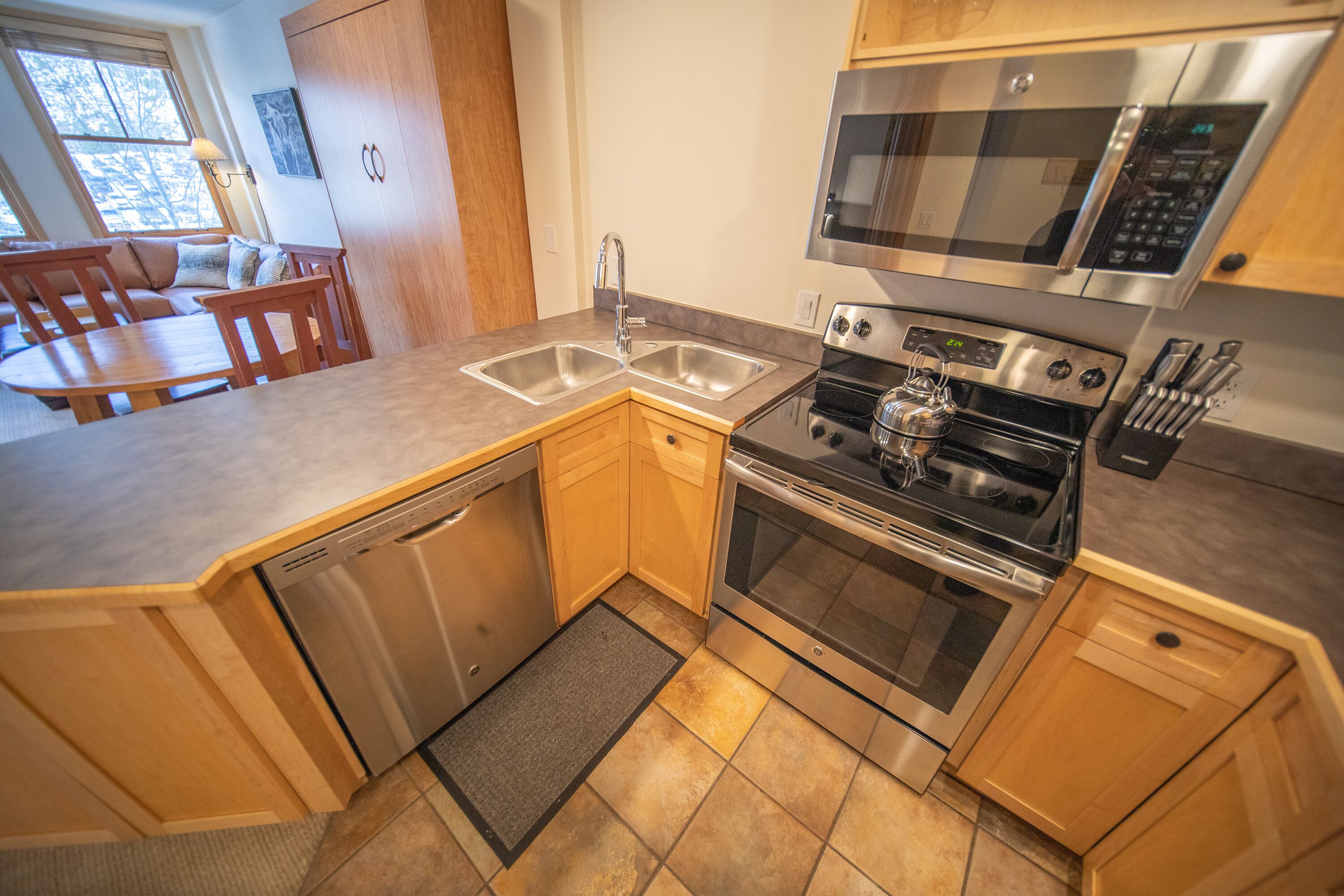A compact kitchen with a dishwasher, double sink, stainless steel oven, microwave, and wooden cabinets.
