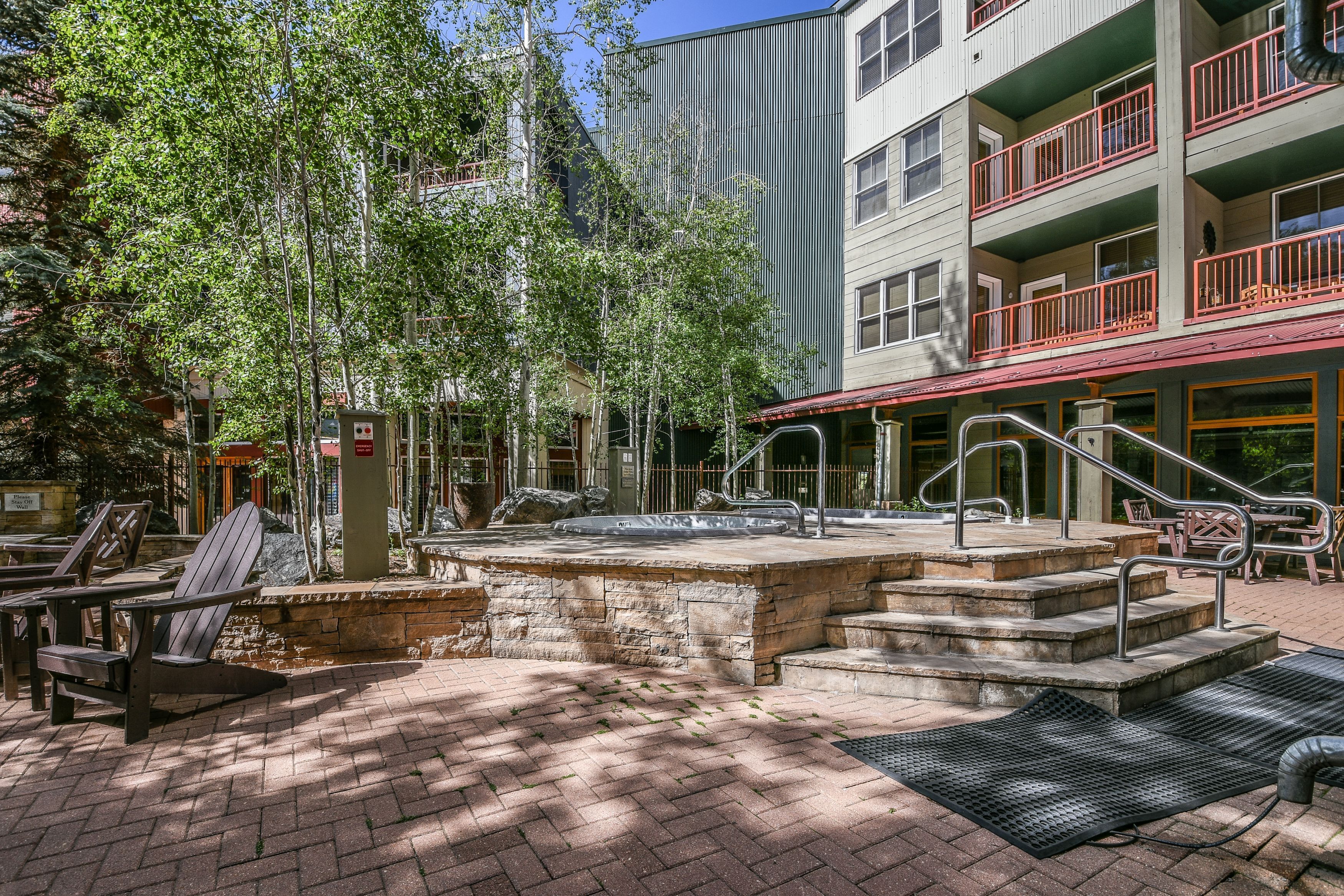 An outdoor patio area with Adirondack chairs, a stone fountain, and a staircase leading to a building with balconies.