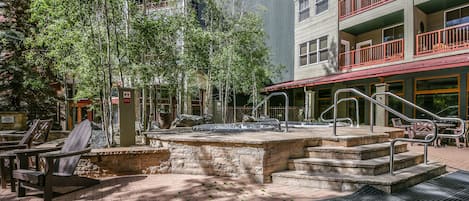 An outdoor patio area with Adirondack chairs, a stone fountain, and a staircase leading to a building with balconies.