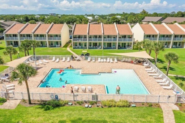 A hotel with a swimming pool surrounded by sun loungers and a fenced area.