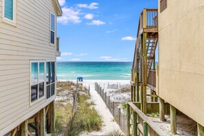 A beachfront property with a wooden deck, a sandy path leading to the beach, and a view of the ocean.