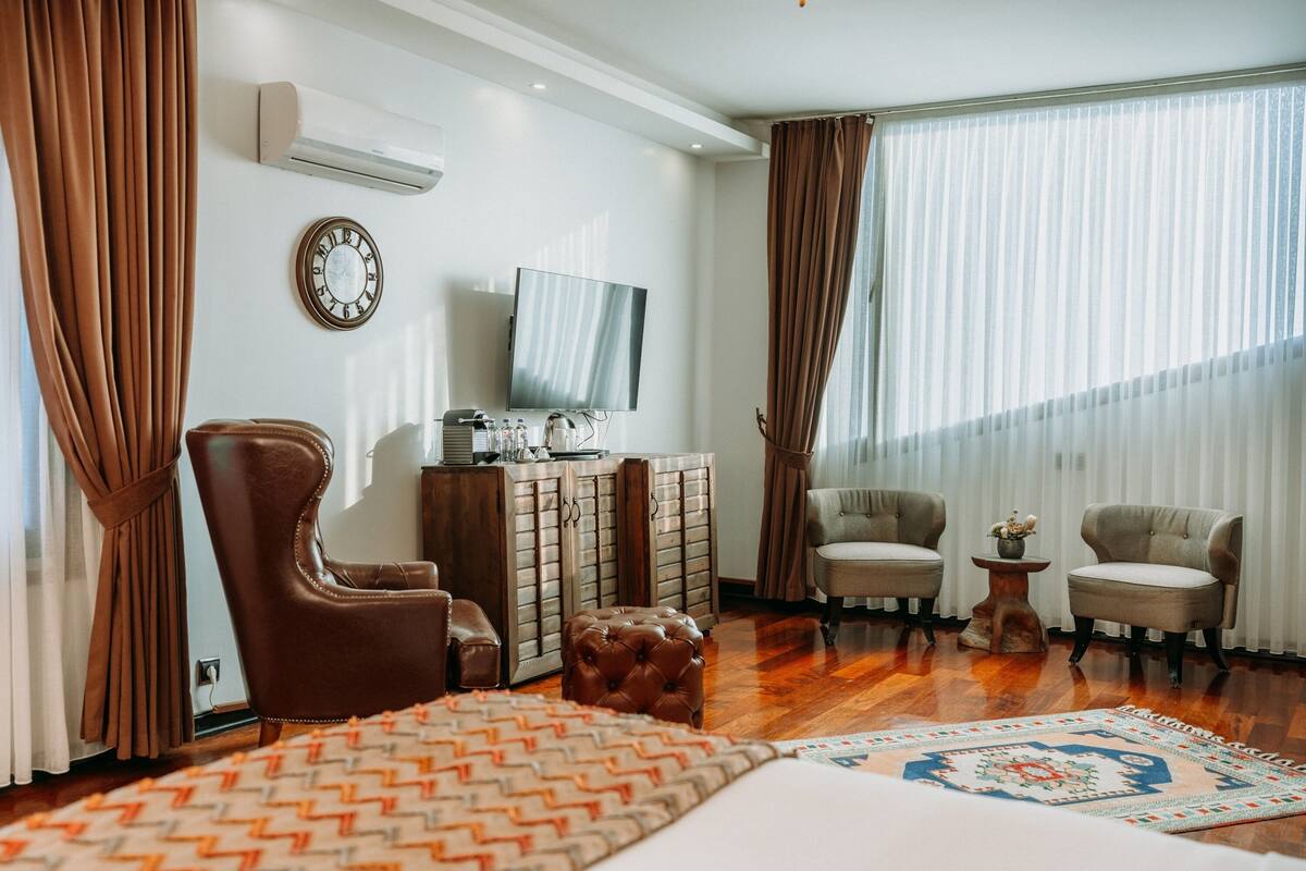 A hotel room with a large bed, two armchairs, a wooden cabinet, a television, and a window with curtains.