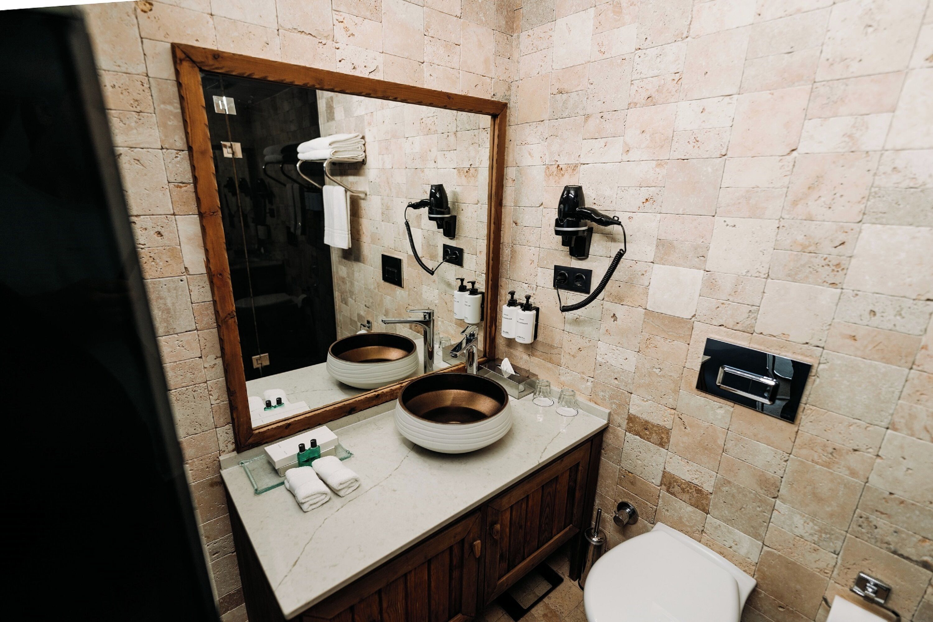 A bathroom with a large mirror, two sinks, a toilet, and a towel rack.