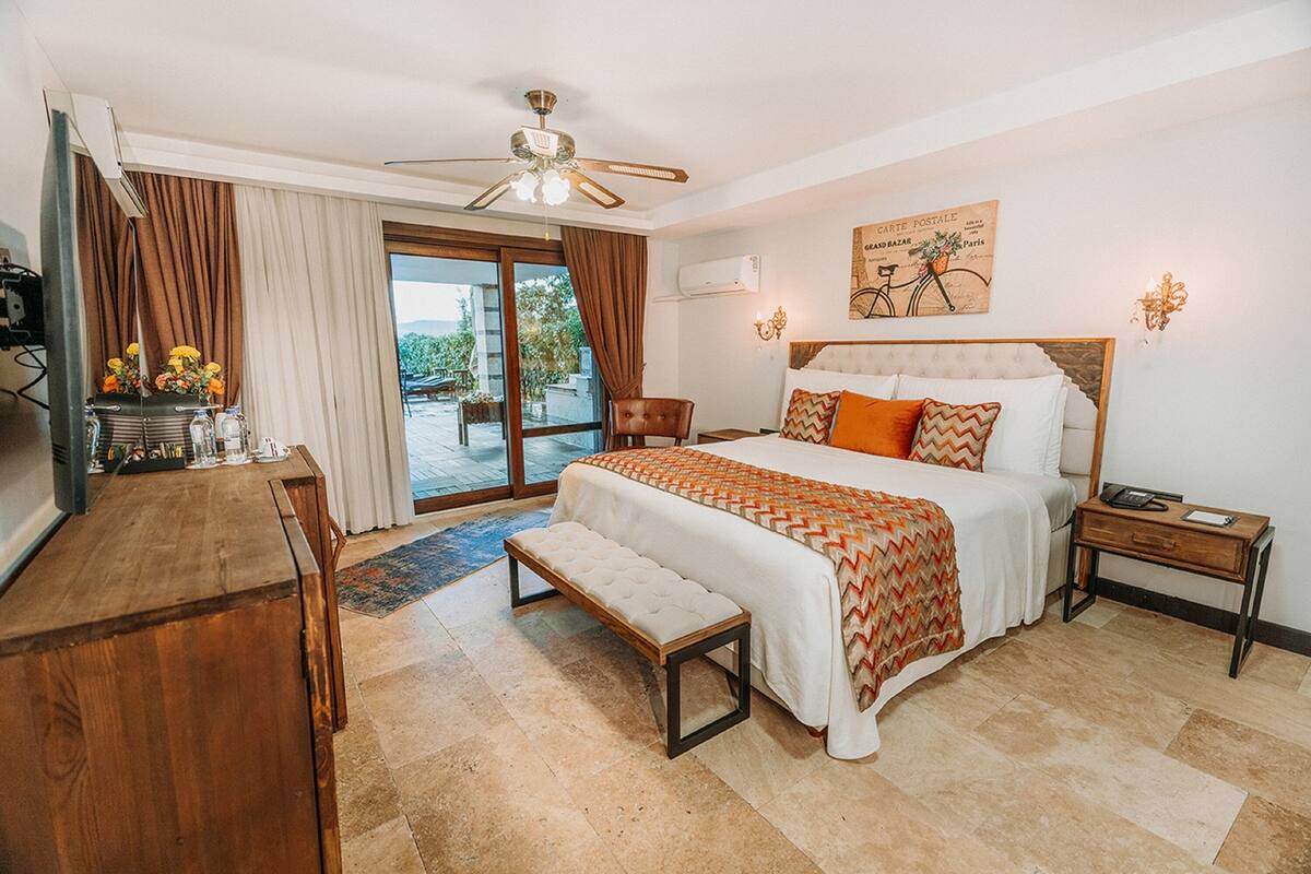 A hotel room with a bed, bench, desk, and a view of the outdoors.