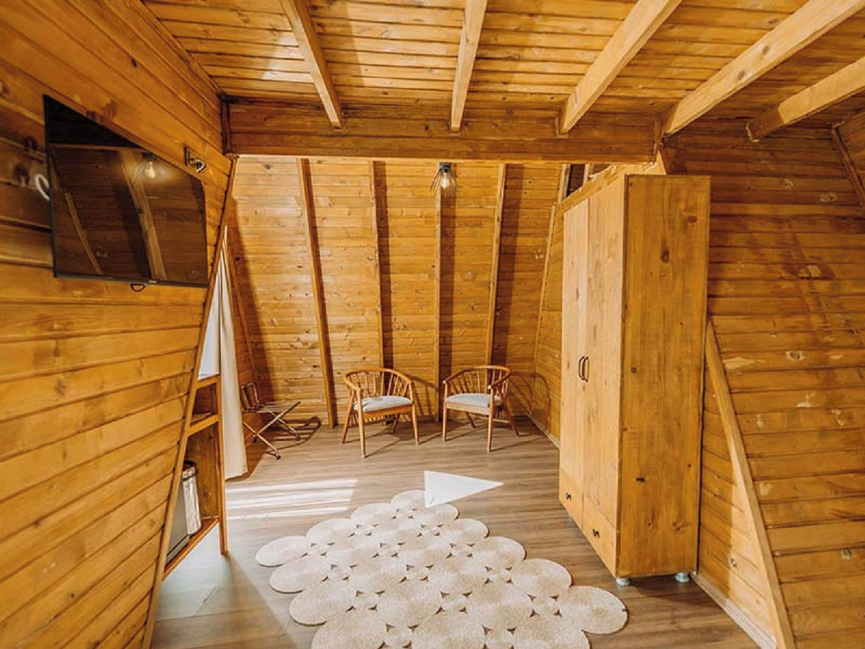 Un intérieur en bois avec un plafond de style industriel, deux chaises en bois, un tapis blanc et un meuble.