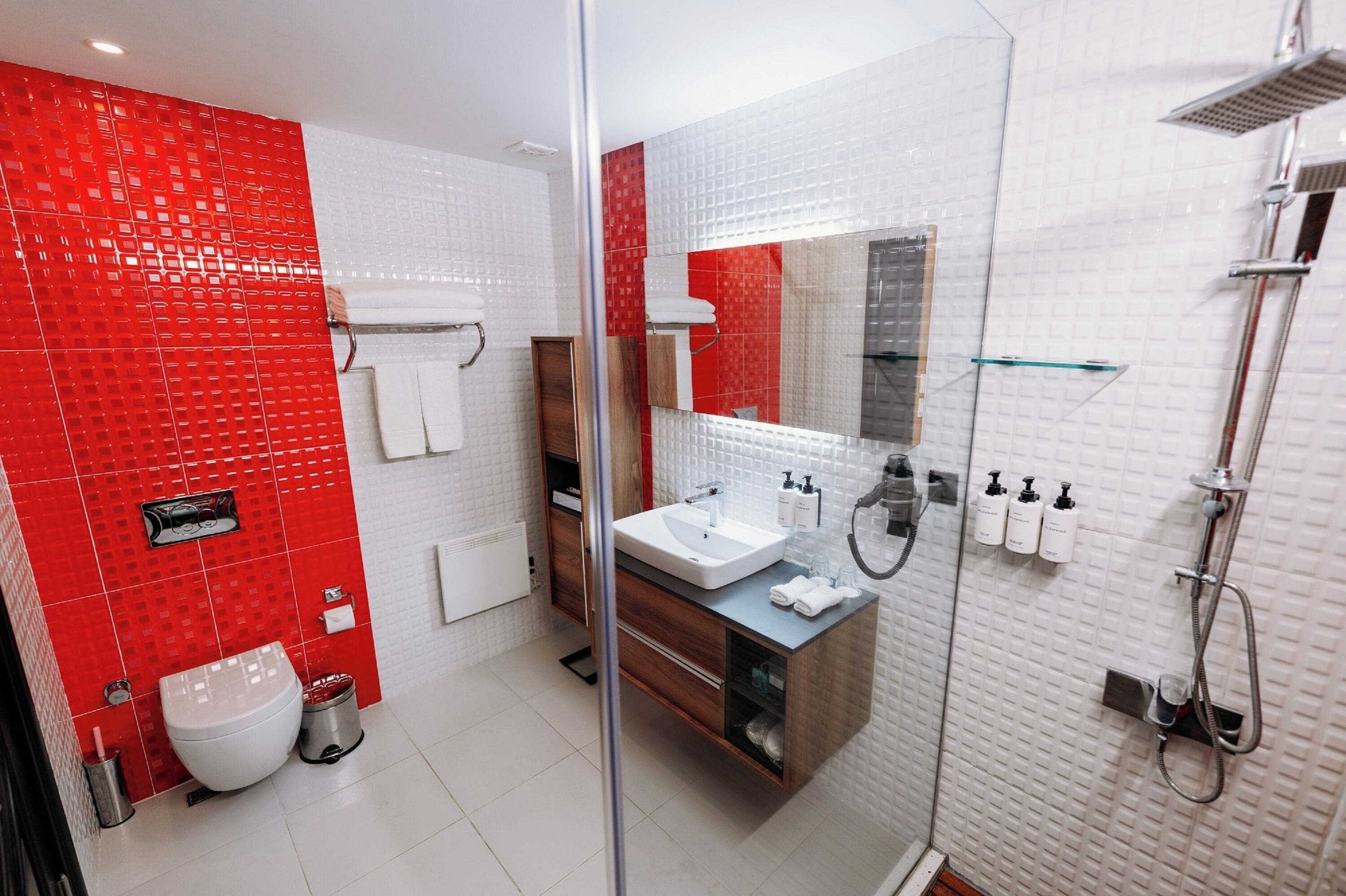 A modern bathroom with a red and white tiled wall, a glass shower enclosure, a sink with a mirror, and a toilet.