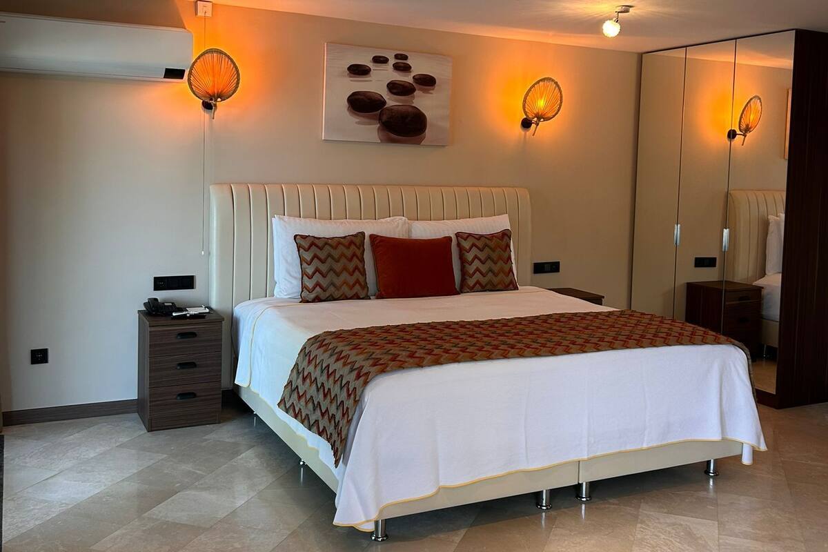 A modern bedroom with a large bed, bedside tables, a mirror, and wall-mounted lighting.