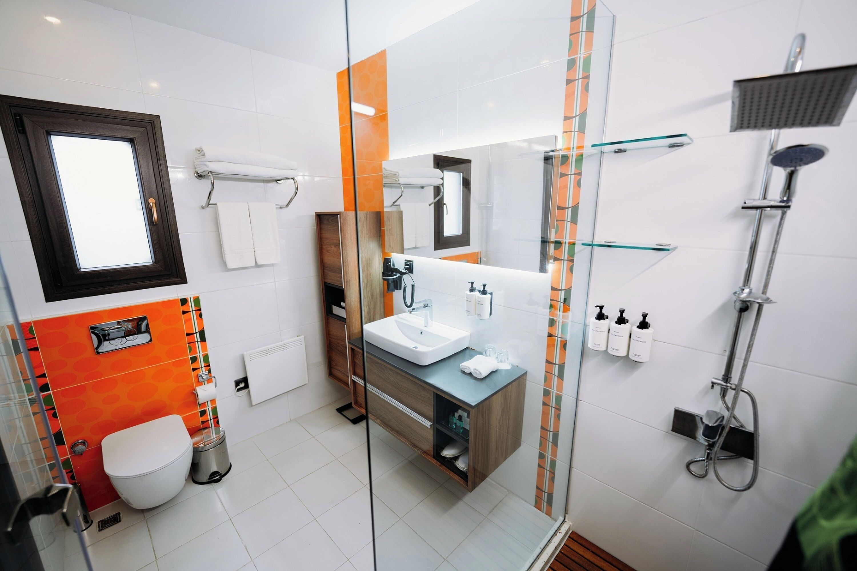 A modern bathroom with a glass shower enclosure, a white toilet, a wooden vanity, and a large mirror.