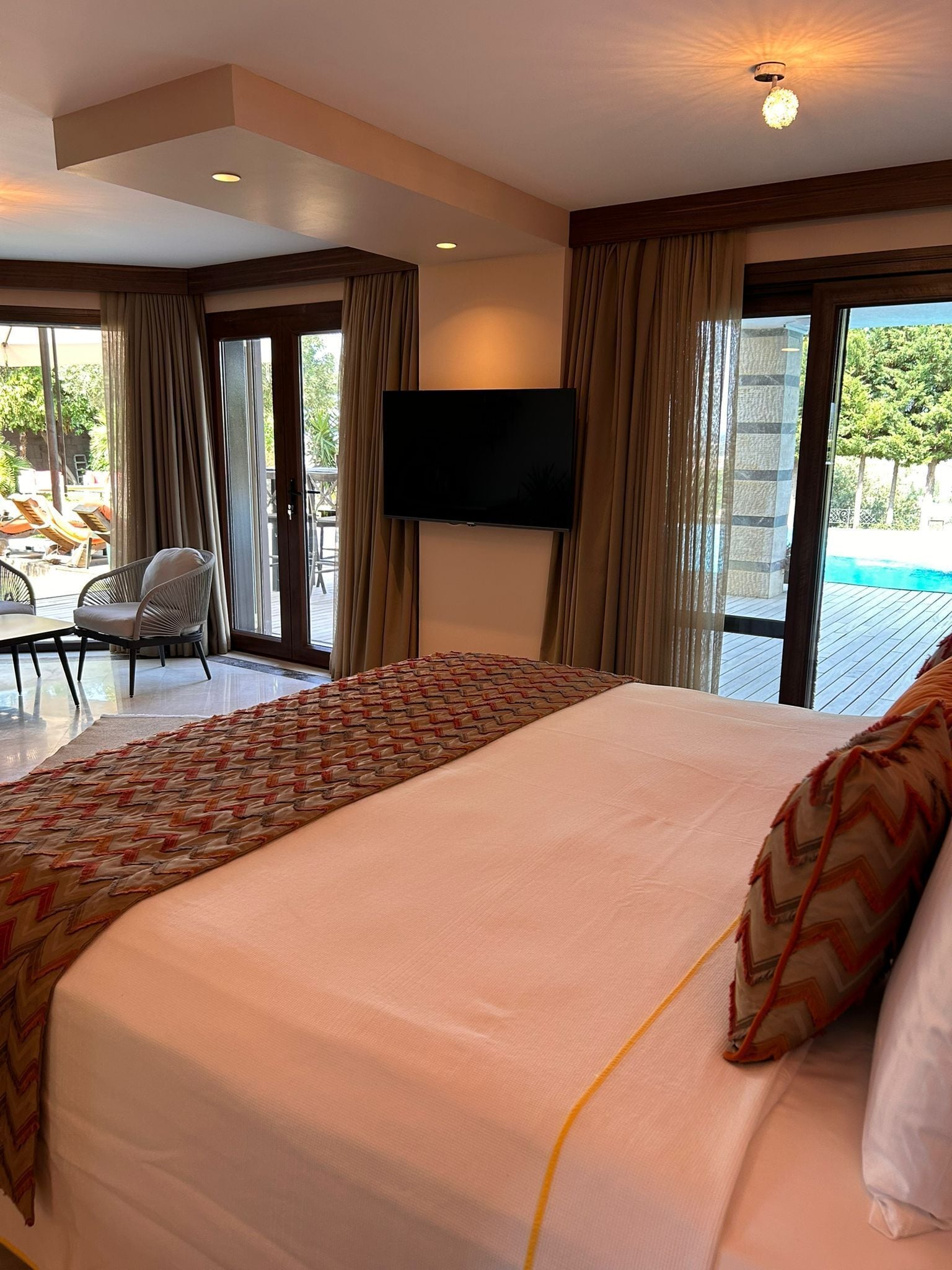 Habitación de hotel con una cama grande, un televisor de pantalla plana montado en la pared y un ventanal corredero que da a un área exterior con piscina.