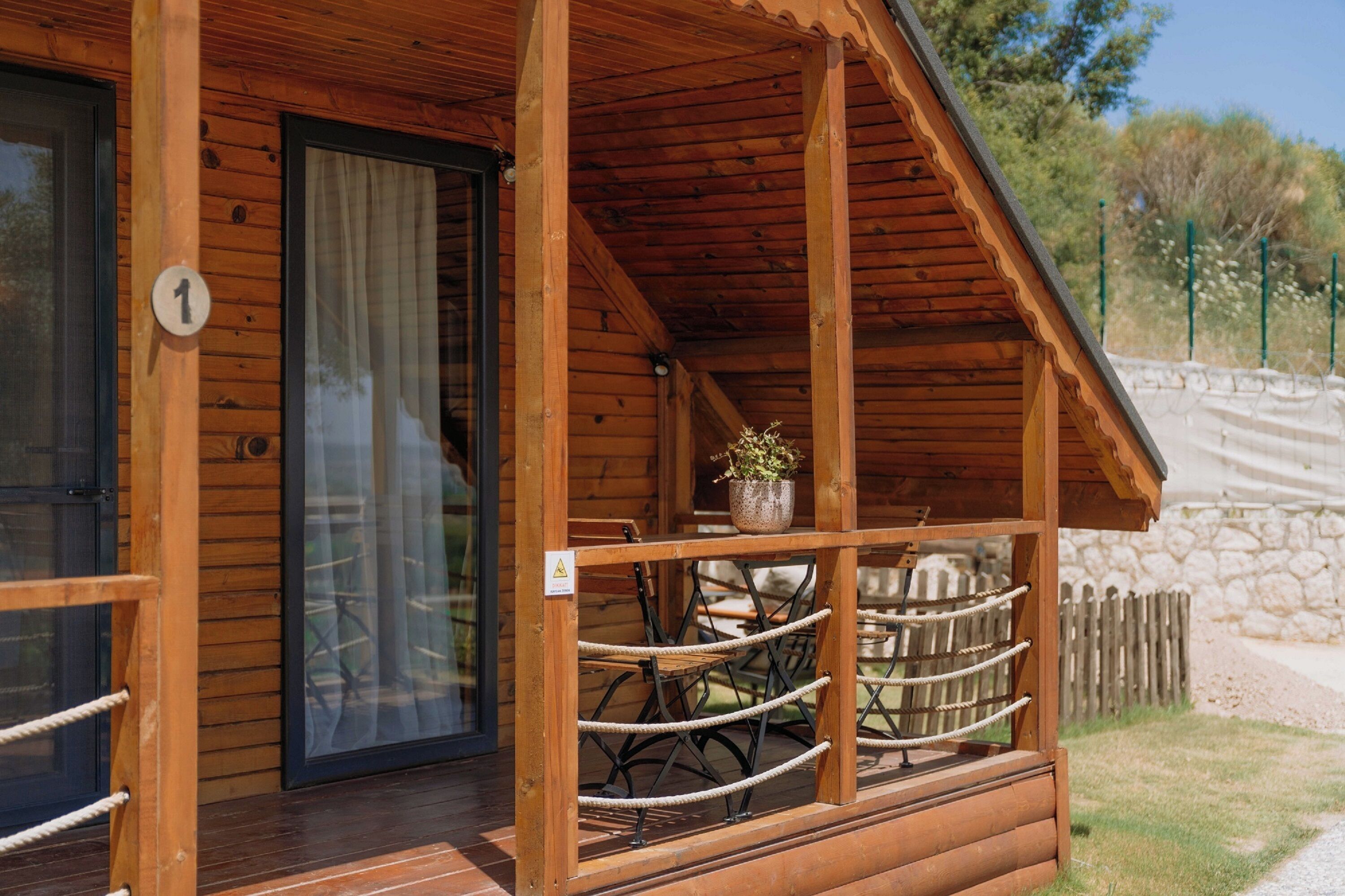 A wooden cabin with a glass door, a small porch with a railing, and a potted plant on the porch.