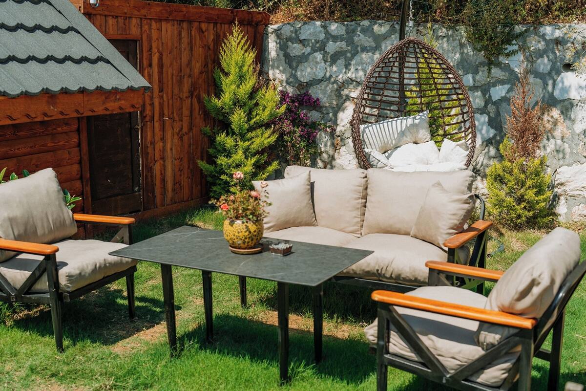 A cozy outdoor seating area with a sofa and chairs, a small table, and a hanging chair.
