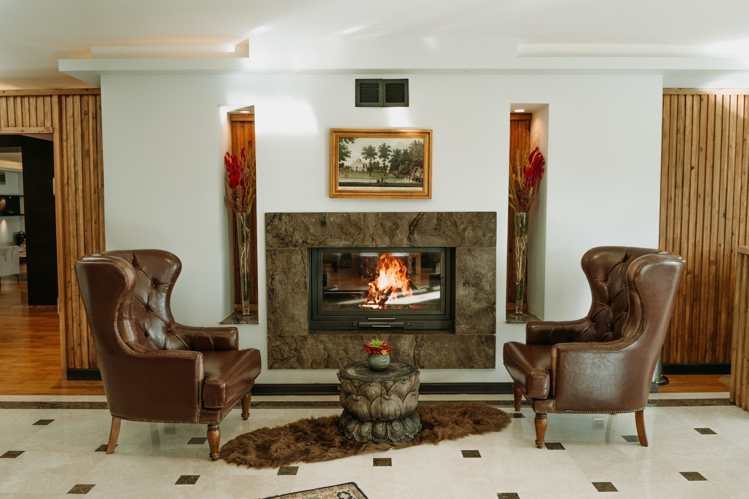 Ein Wohnzimmer mit Kamin, zwei Ledersessel, einem runden Holztisch und einem gerahmten Bild über dem Kamin.