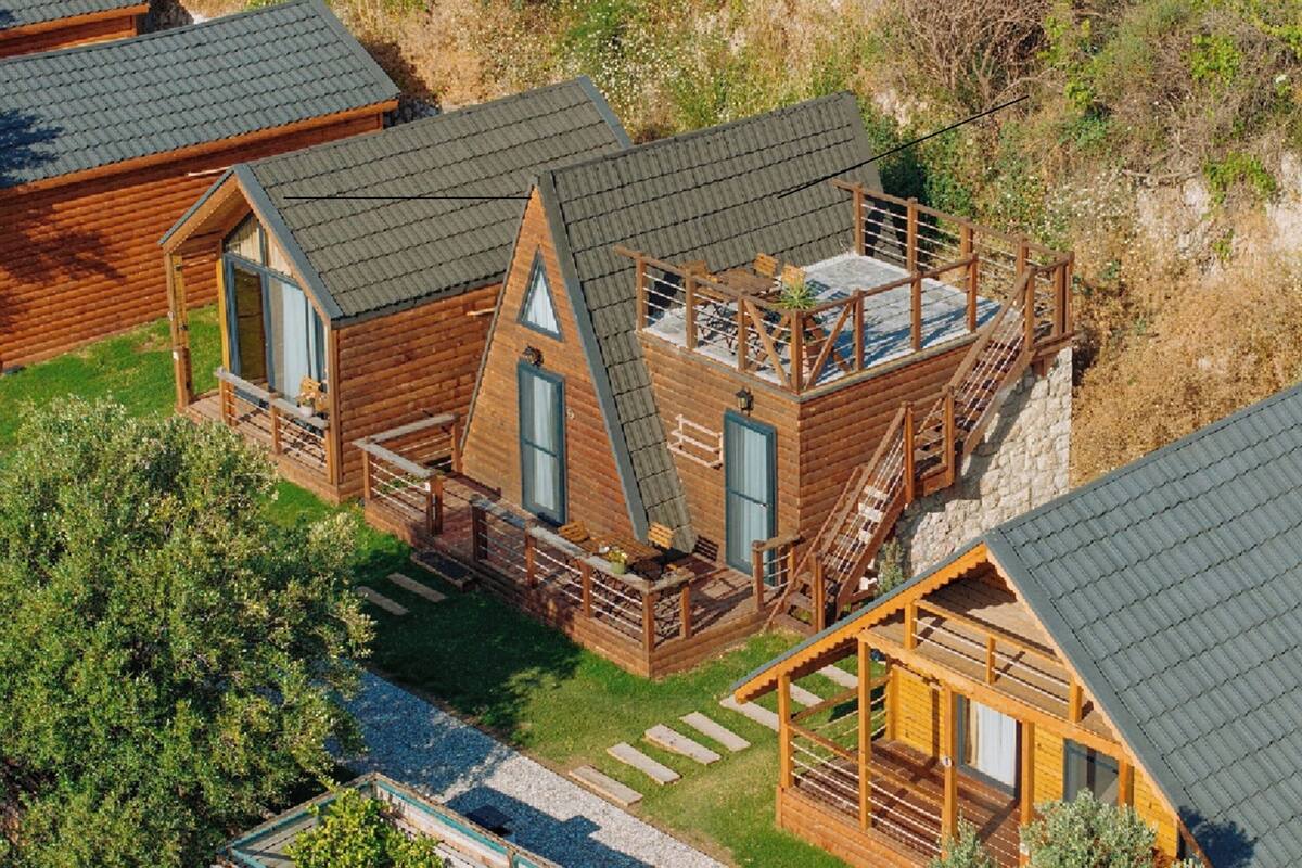 A wooden cabin with a steeply pitched roof, a balcony, and a small porch area.