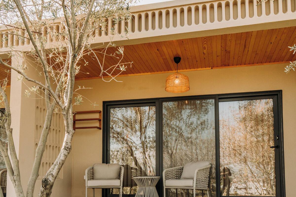A patio with two chairs and a table, a stone wall, and a tree.