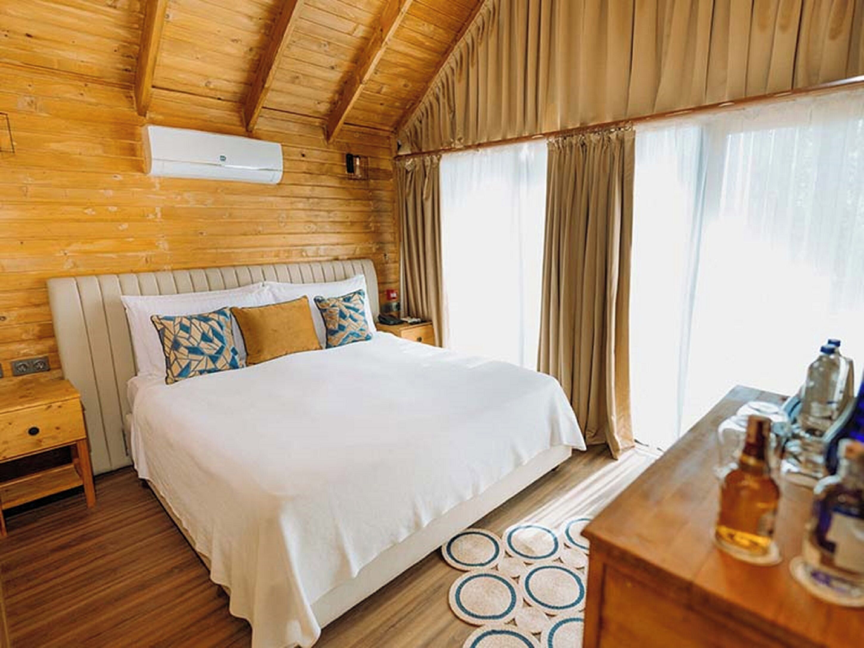 A wooden room with a bed, nightstands, and a window with curtains.