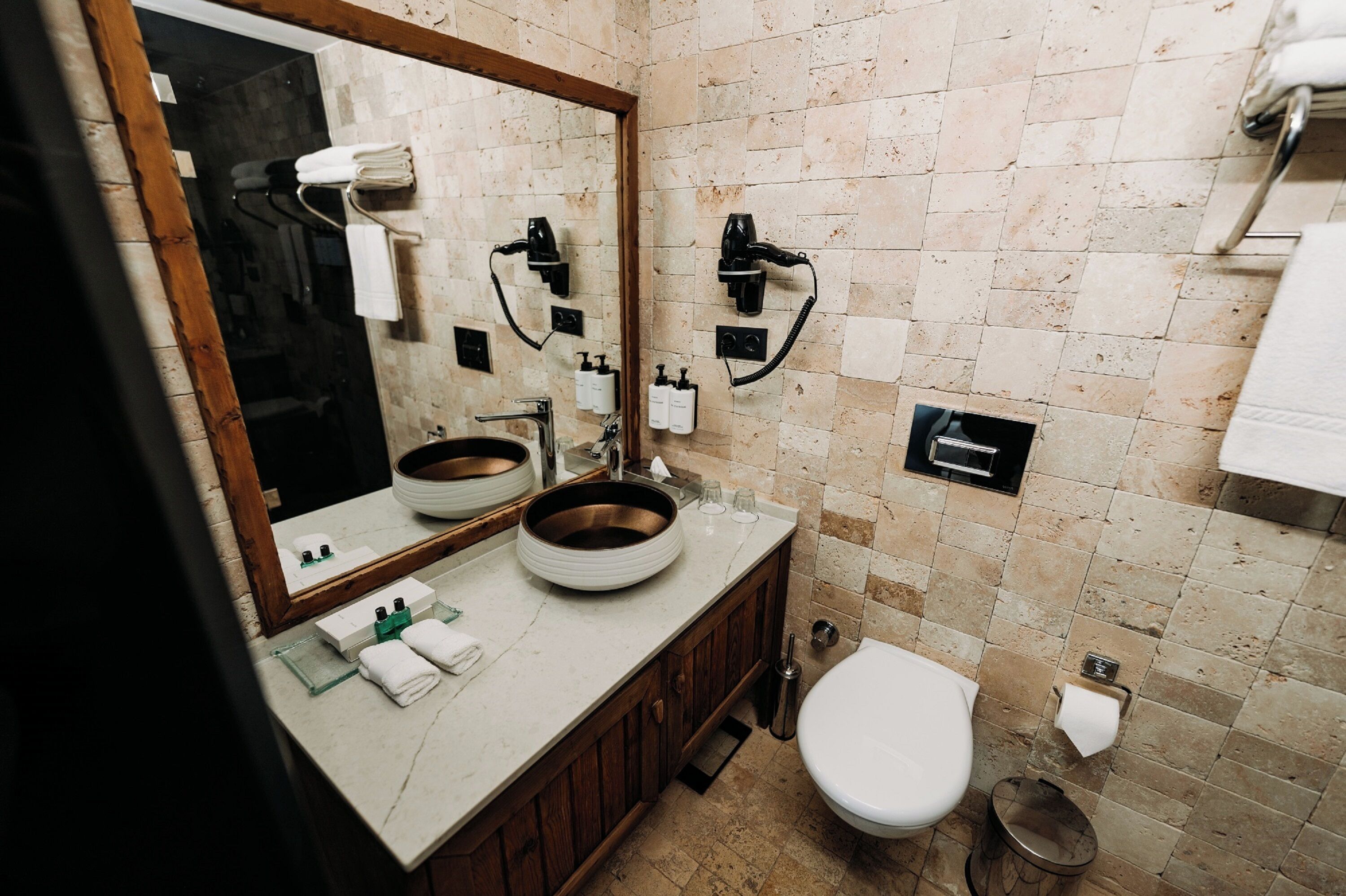 A bathroom with a large mirror, a round sink, a toilet, and a shower area.