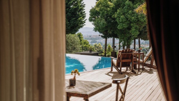 A wooden deck with a pool, outdoor furniture, and a view of trees and buildings. - Doors Urla Hotel & Bungalows (Urla)