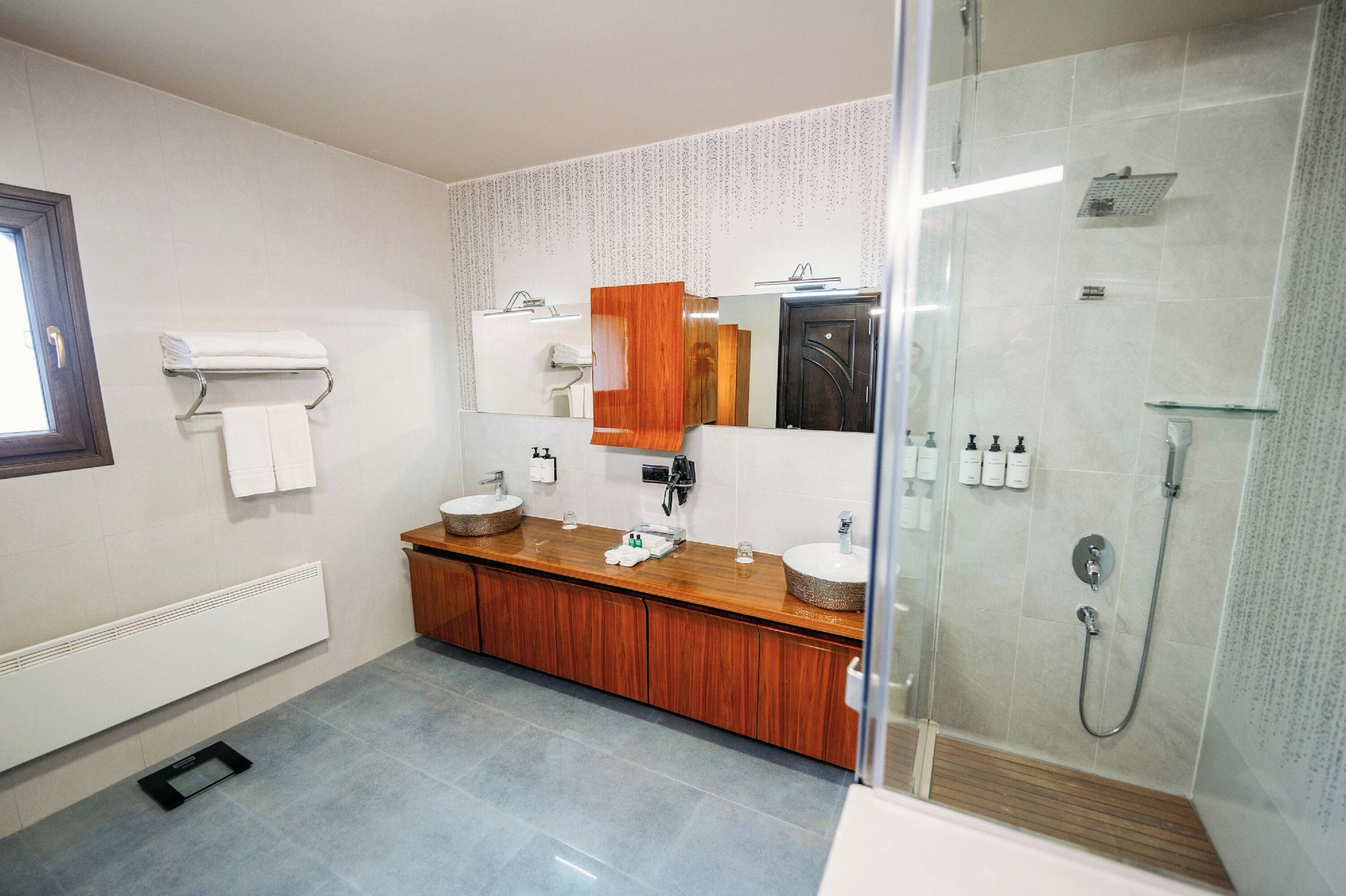 A modern bathroom with a wooden vanity, two sinks, a glass shower enclosure, and a towel rack.