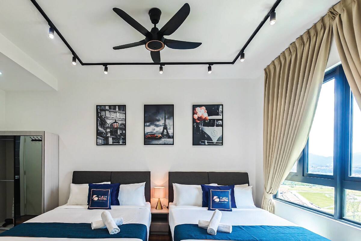 A hotel room with two beds, a ceiling fan, and artwork on the walls.