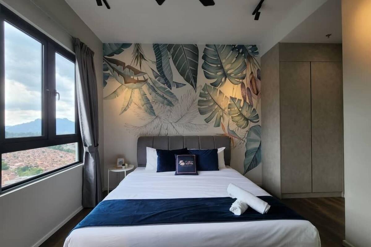 A hotel room with a bed, a nightstand, a large window, and a tropical leaf mural on the wall.