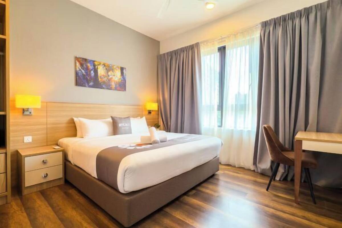 A hotel room with a large bed, bedside tables with lamps, a desk, and a painting on the wall.