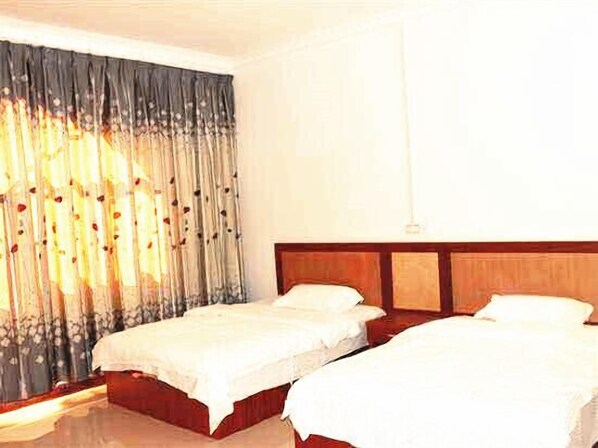 A hotel room with two beds, a wooden headboard, and a large window with curtains.