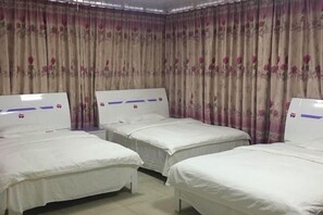A hotel room with three single beds, a large window with curtains, and a plain wall.