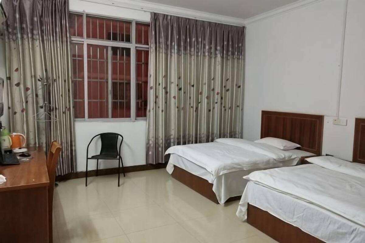 A hotel room with two beds, a desk, a chair, and a window with curtains.