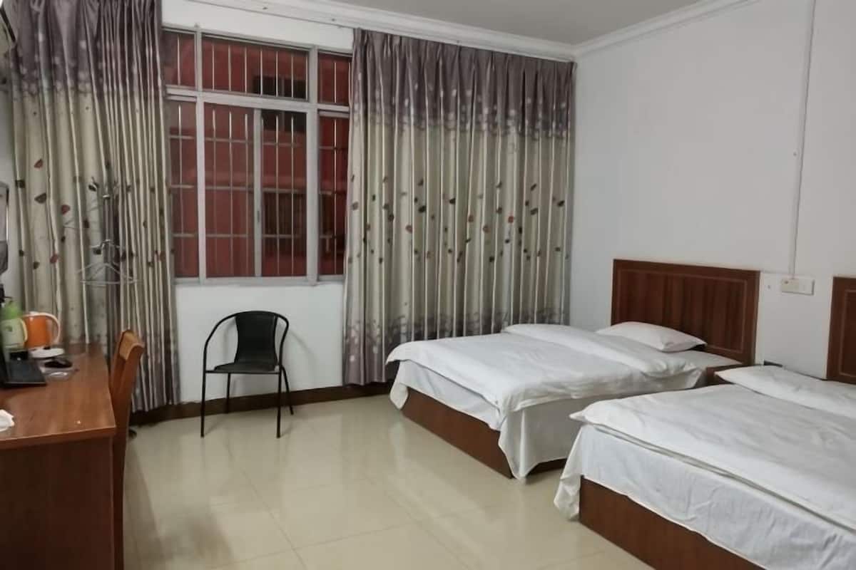 A hotel room with two beds, a desk, a chair, and a window with curtains.