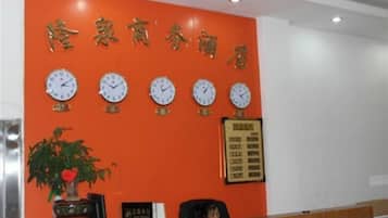 Un área de recepción con un reloj de pared, un cartel enmarcado y una planta en maceta.