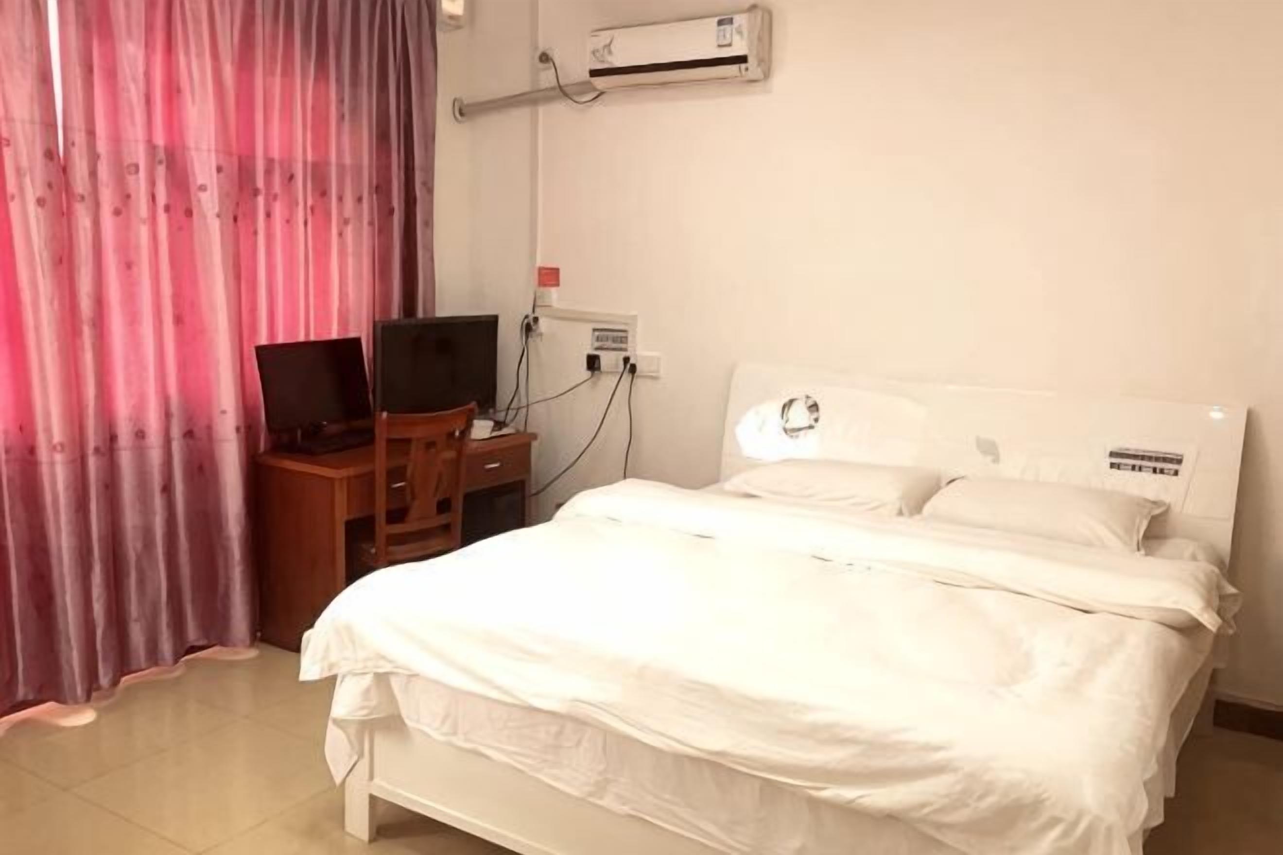 A hotel room with a bed, a desk with a computer, and an air conditioning unit.