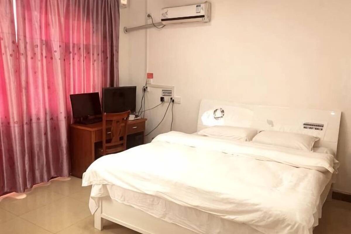 A hotel room with a bed, a desk with a computer, and an air conditioning unit.