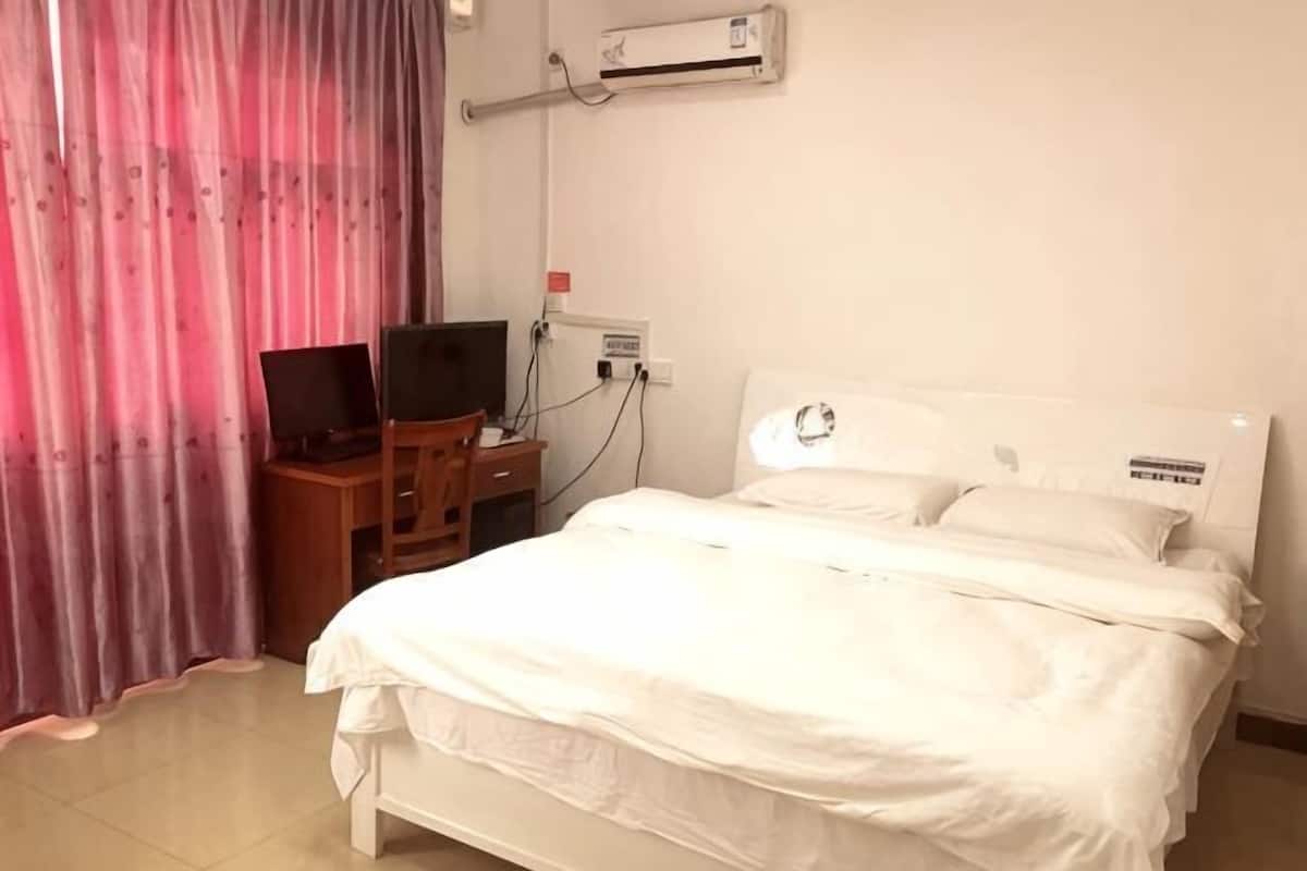 A hotel room with a bed, a desk with a computer, and an air conditioning unit.