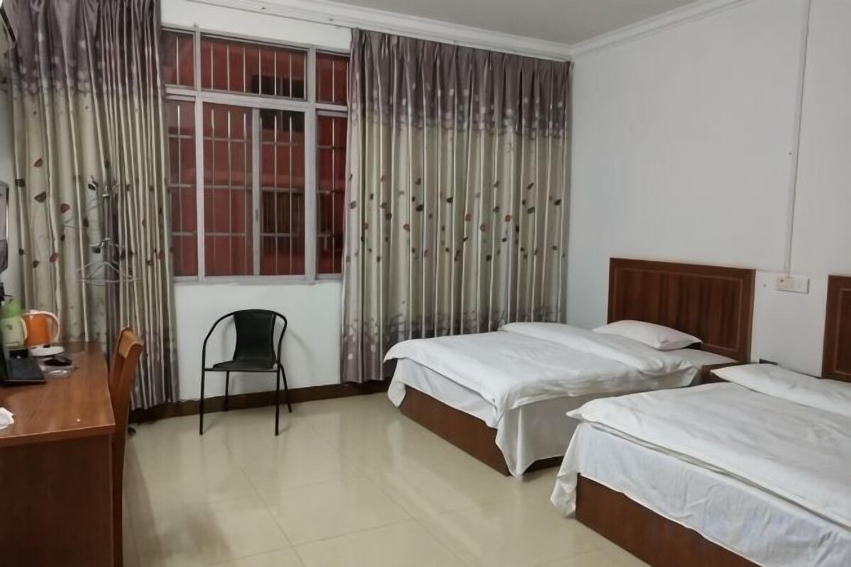 A hotel room with two beds, a desk, a chair, and a window with curtains.
