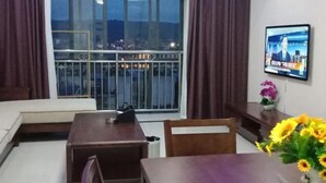 A hotel room with a balcony, a TV mounted on the wall, a dining table, and a chair. - Yashige Apartment Ruili (Ruili)