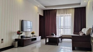 A modern living room with a flat-screen TV, a dark sofa, a coffee table, and a large window with curtains. - Yashige Apartment Ruili (Ruili)