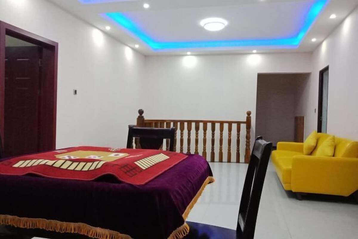Una habitación con una cama, un sofá amarillo, una silla de madera y una mesita.