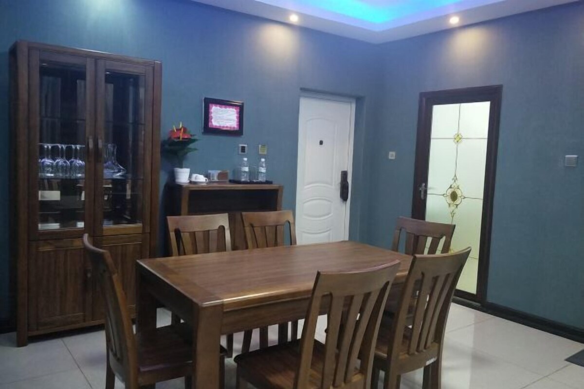 Un comedor con una mesa y sillas de madera, un armario con puertas de vidrio, una puerta blanca y una pequeña planta.