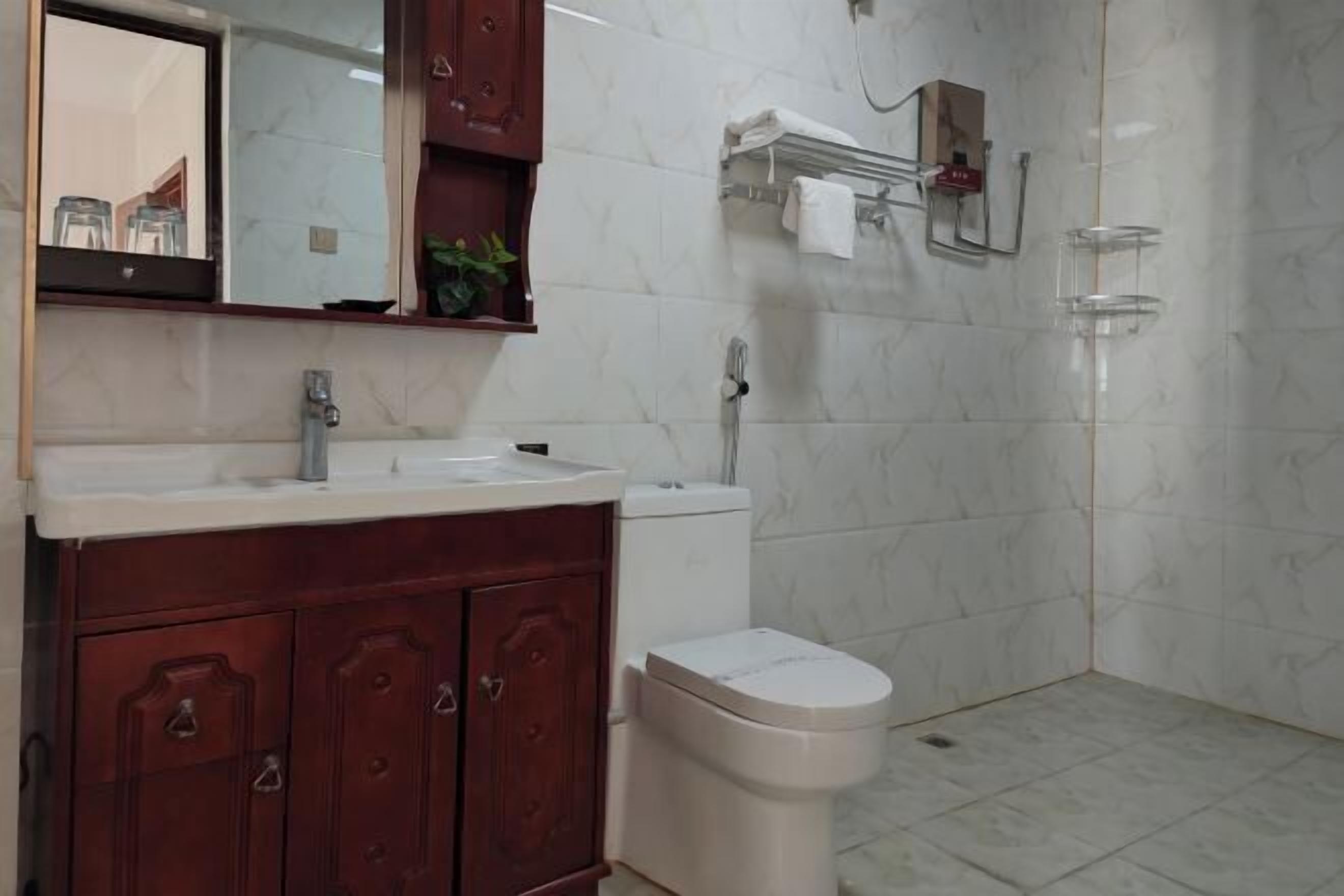 A bathroom with a wooden vanity, a white sink, a toilet, and a shower area.