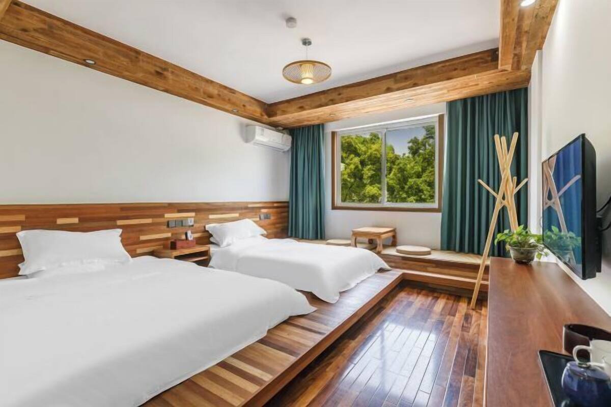 Habitación de hotel con dos camas, vigas de madera, una ventana con vistas, un televisor y una mesita.