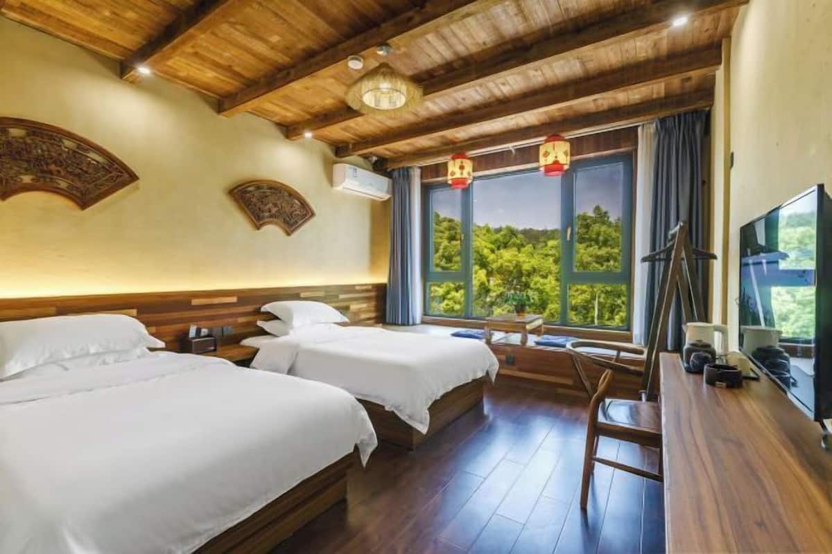 Habitación de hotel con dos camas, techo de madera, ventana grande con vistas y escritorio con televisor.