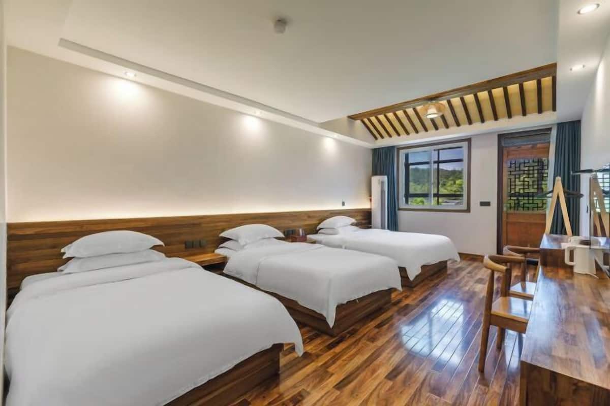 Habitación de hotel con tres camas, piso de madera, un escritorio con sillas y vistas al exterior.