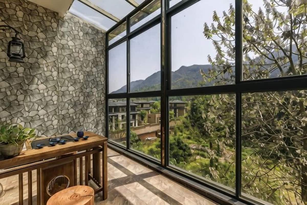 Una habitación con pared de piedra, una mesa de madera con sillas y un ventanal con vistas a la vegetación y montañas.