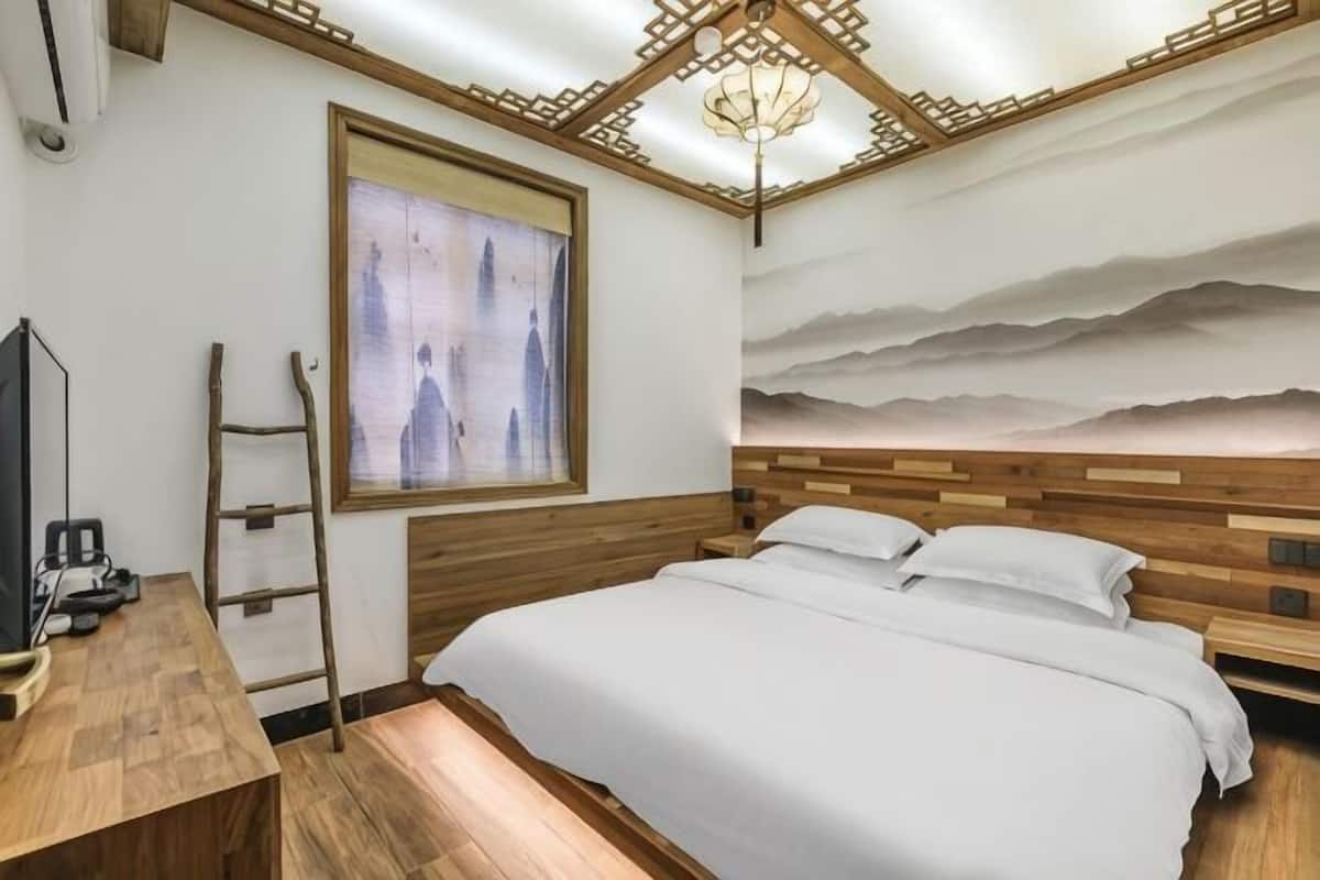 Un dormitorio con cabecera de madera, cama con ropa de cama blanca, un escritorio con silla, una escalera, un televisor y un ventanal grande.